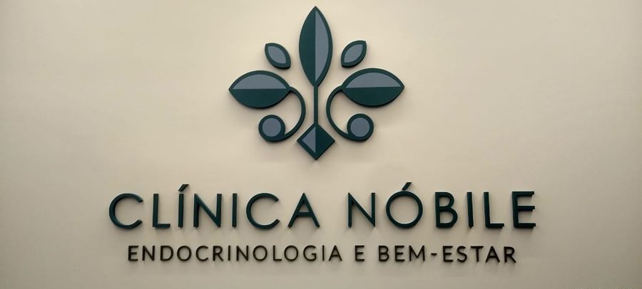Logotipo Clínica Nóbile em acrílico recortado, verde petróleo sobre parede clara